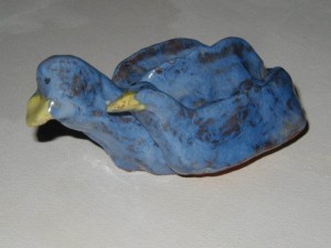 Ceramic sculpture of two blue birds, one larger and one smaller, nestled together with yellow beaks.