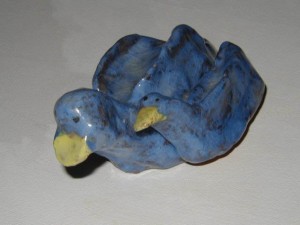 Ceramic sculpture of two blue birds, one larger and one smaller, nestled together with yellow beaks.