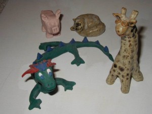 Group of five small clay animal figurines including a green dragon, a spotted giraffe, a pink pig, a brown cat, and a bird-like creature.