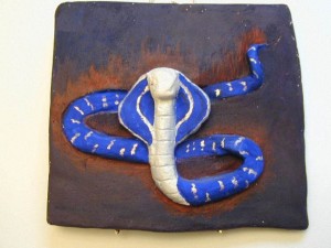 Clay relief sculpture of a blue and white cobra on a brown and black rectangular background.