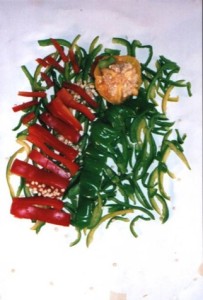 Sliced red and green bell peppers arranged in rows with seeds and a yellow pepper top, laid out on a white background.