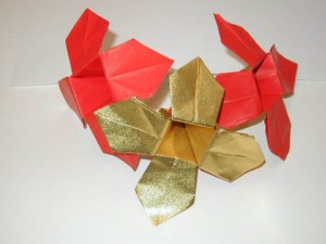 Close-up of three origami flowers; two are red with gold inner petals, and one features fully metallic gold petals.