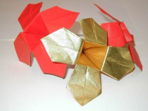Close-up of three origami flowers; two are red with gold inner petals, and one features fully metallic gold petals.