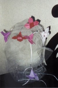 Mesh structure adorned with small origami butterflies in red, purple, and white, attached via thin wires or strings.