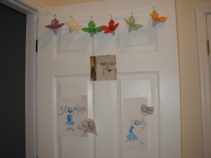 White door decorated with colorful origami butterflies and labeled paper signs reading “Stephanie” and “Candy,” along with a small center poster.