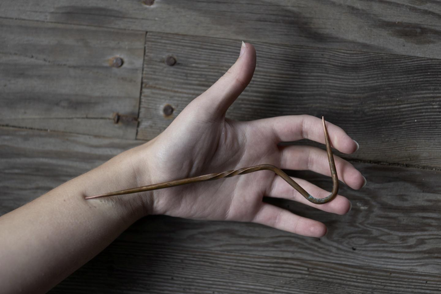 A hand, with a copper spike pressing on it